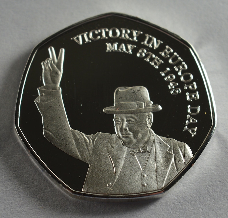 May include: Silver coin commemorating Victory in Europe Day, May 8th, 1945. The coin features a portrait of Winston Churchill raising his hand in a victory salute.