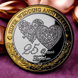 Op de afbeelding: Zilveren munt met een gouden rand, met twee in elkaar verweven harten met ingewikkelde ontwerpen. De munt heeft de tekst "Silver Wedding Anniversary 25 Years Together".
