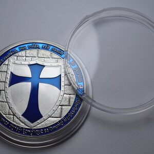 K&ouml;nnte beinhalten: Eine silberne M&uuml;nze mit einem blauen Kreuz auf einem Schild, umgeben von einer Ziegelmauer. Die M&uuml;nze befindet sich in einem durchsichtigen Plastiketui. Der Text auf der M&uuml;nze lautet "non nodie numine, nun vuldix, sed nomine", "Deuger" und "semper cum fiducia salomunic hicrusjemiton".