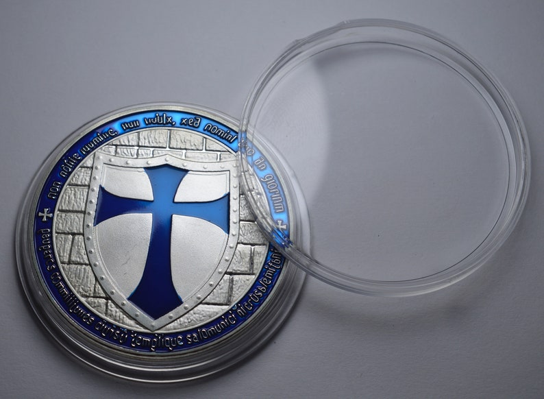 K&ouml;nnte beinhalten: Eine silberne M&uuml;nze mit einem blauen Kreuz auf einem Schild, umgeben von einer Ziegelmauer. Die M&uuml;nze befindet sich in einem durchsichtigen Plastiketui. Der Text auf der M&uuml;nze lautet "non nodie numine, nun vuldix, sed nomine", "Deuger" und "semper cum fiducia salomunic hicrusjemiton".