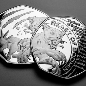 Könnte beinhalten: Zwei silberne Münzen mit einem Motiv eines mythischen Tieres, der Bestie von Bodmin, einer Kreatur, von der man glaubt, dass sie in der Bodmin Moor in Cornwall, Großbritannien, lebt. Der Text auf der Münze lautet "The Beast of Bodmin" und "Cornwall UK. Bodmin Moor became the centre of reports of mutilated animals."