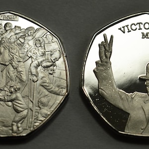May include: A silver commemorative coin celebrating Victory in Europe Day, May 8th, 1945. One side features a crowd of people celebrating, while the other side shows Winston Churchill giving a victory salute.