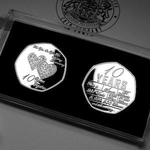 Può includere: Due monete commemorative d'argento in una custodia di plastica trasparente. La moneta a sinistra presenta due cuori intrecciati con la scritta "10 Years Together". La moneta a destra ha la scritta "10 Years" e un elenco di date.