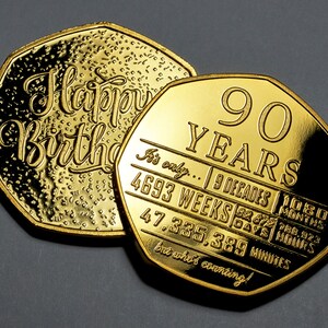 May include: Two gold-coloured coins with a 90th birthday message. The top coin says "Happy Birthday" and the bottom coin says "90 Years" and lists the number of decades, weeks, days, hours, and minutes in 90 years. The text on the bottom coin reads "It's only... 9 Decades | 1080 Months | 4693 Weeks | 32,672 Days | 788,928 Hours | 47,335,389 Minutes but who's counting!"