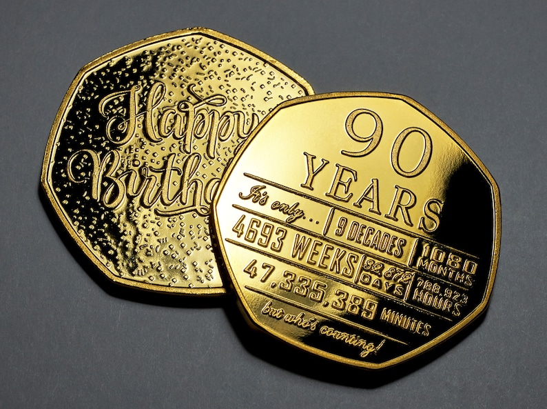 May include: Two gold-coloured coins with a 90th birthday message. The top coin says "Happy Birthday" and the bottom coin says "90 Years" and lists the number of decades, weeks, days, hours, and minutes in 90 years. The text on the bottom coin reads "It's only... 9 Decades | 1080 Months | 4693 Weeks | 32,672 Days | 788,928 Hours | 47,335,389 Minutes but who's counting!"