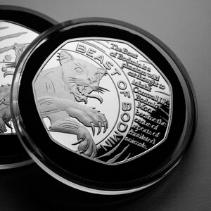 Könnte beinhalten: Eine Silbermünze mit einem Schwarzweißbild einer Wildkatze und dem Text "The Beast of Bodmin is a phantom wild cat thought to inhabit Cornwall UK Bodmin Moor became the centre of reports of mutilated animals."