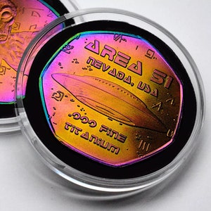 May include: A gold-toned coin with a holographic finish features a UFO and the text "Area 51 Nevada, USA" and "999 Fine Titanium".