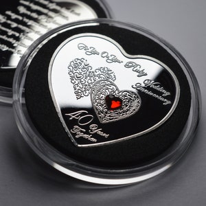 May include: A silver heart-shaped coin with a red ruby gemstone in the centre. The coin is engraved with "For You On Your Ruby Wedding Anniversary 40 Years Together".