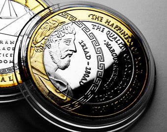 May include: A silver and gold coin with a portrait of a man on one side and the text "THE HAPPINESS OF THE QUALITY OF" on the other side.