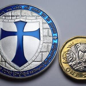 K&ouml;nnte beinhalten: Eine Silberm&uuml;nze mit einem blauen Kreuz auf einem Schild und dem Text "non adfile tuumine. Hun ix, xe nominl tuo an gloria - peugeres commilitumes cruist templique salomunici nicrust/emitonis" am Rand. Eine Goldm&uuml;nze mit einer Distel, einer Rose und einem Kleeblatt und dem Text "ONE POUND" ist ebenfalls zu sehen.