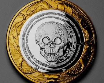 May include: A gold coin with a detailed design of a skull with a silver finish. The skull has a detailed design with a prominent nose and eye sockets.