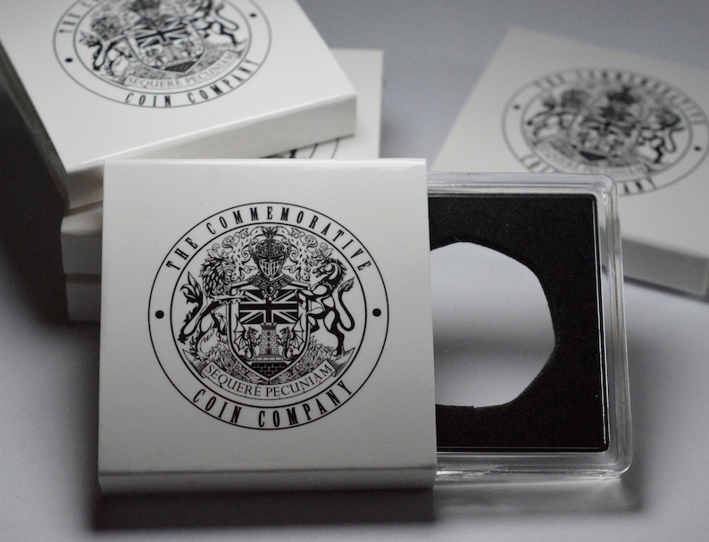 May include: A white coin case with a black and white logo that says "The Commemorative Coin Company" and a black and white crest with the words "Sequere Pecuniam". The case is open and a clear plastic coin holder is visible.
