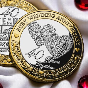 May include: A gold and silver coin commemorating a 40th wedding anniversary. The coin features the words "Ruby Wedding Anniversary" and "40 Years Together." Two ornate hearts are in the center. The coin is on a white background.