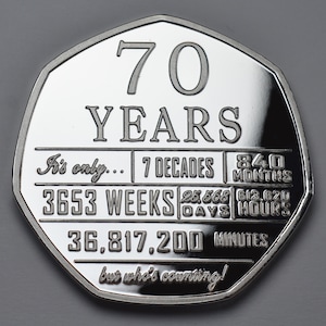 May include: A silver coin with a commemorative design celebrating 70 years. The coin features the text "70 YEARS" and a breakdown of the time period in decades, weeks, days, hours, and minutes. The inscription reads "It's only... 7 Decades 840 Months 3653 Weeks 25,568 Days 613,620 Hours 36,817,200 Minutes but who's counting!"