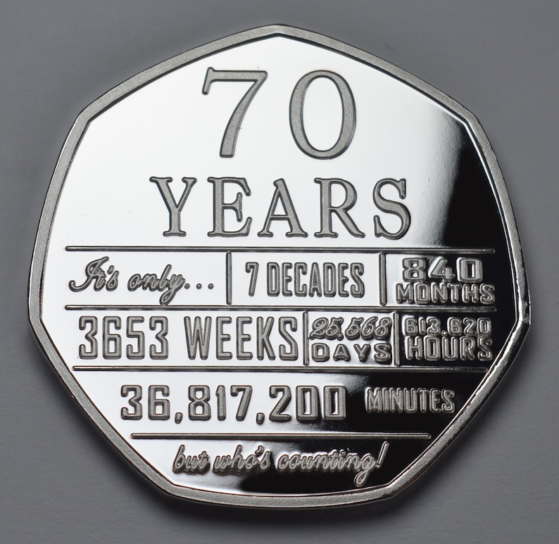 May include: A silver coin with a commemorative design celebrating 70 years. The coin features the text "70 YEARS" and a breakdown of the time period in decades, weeks, days, hours, and minutes. The inscription reads "It's only... 7 Decades 840 Months 3653 Weeks 25,568 Days 613,620 Hours 36,817,200 Minutes but who's counting!"