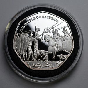 May include: A silver coin depicting the Battle of Hastings. The coin shows Norman knights on horseback charging into battle against Anglo-Saxon warriors. The coin is inscribed with the words "The Battle of Hastings".