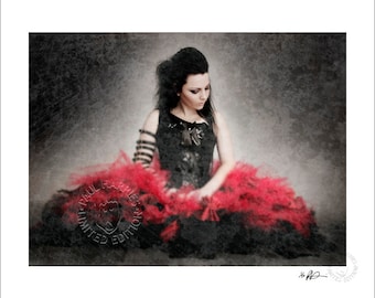May include: A woman in a black dress with a red feather boa sits on a textured gray background. The image has a vintage, faded look.