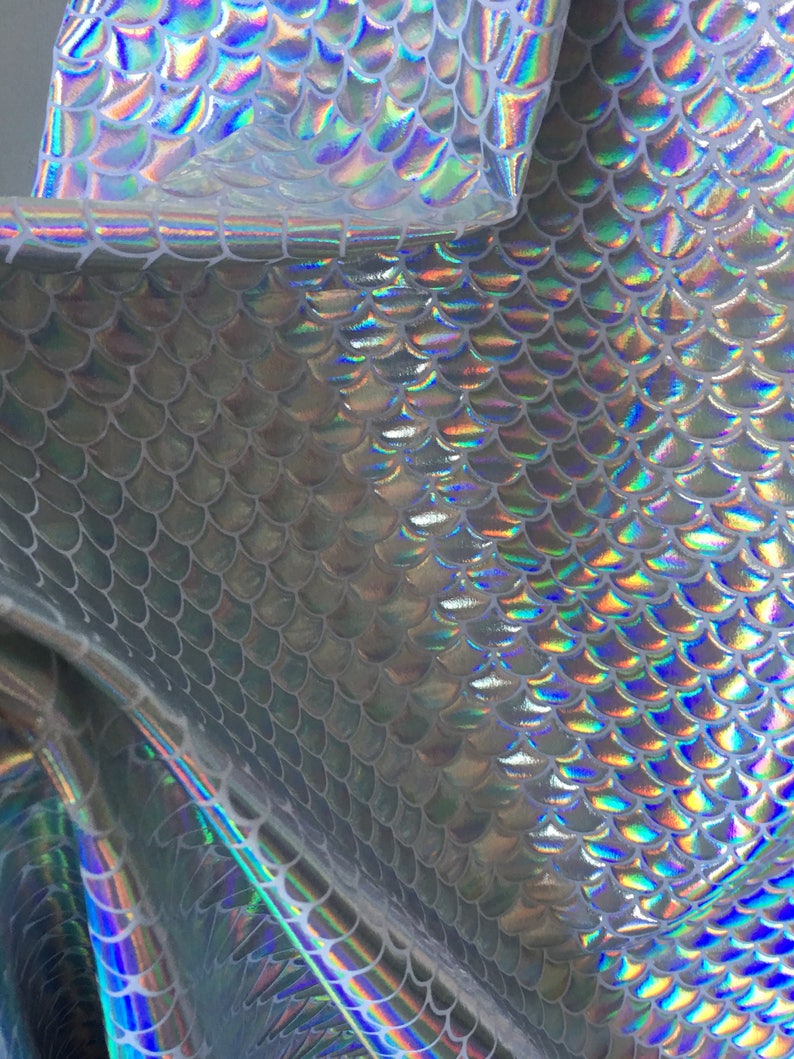 May include: Silver iridescent fabric with a mermaid scale pattern. The fabric is shiny and has a holographic effect.