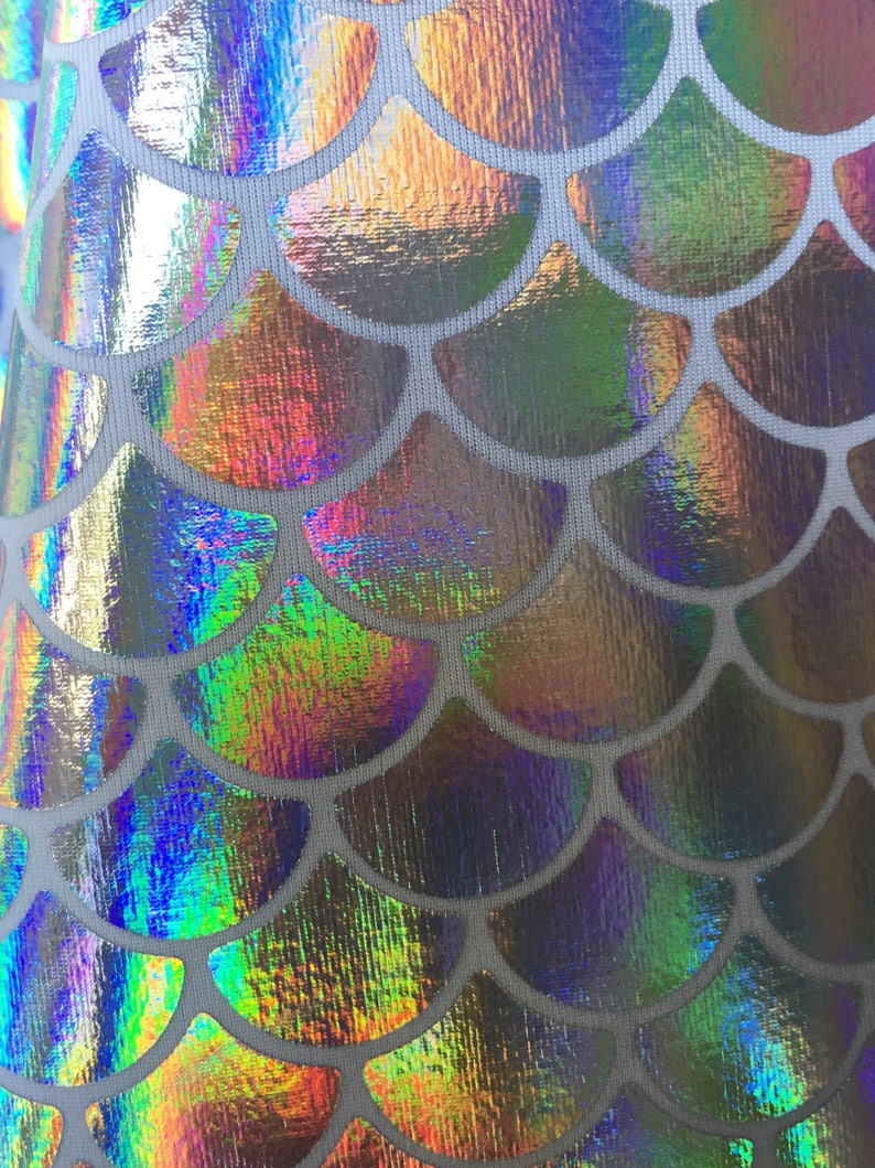 May include: Close-up of iridescent fabric with a mermaid scale pattern. The scales are a holographic silver color with a rainbow sheen.