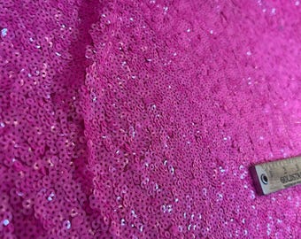 May include: Close-up of a bright pink fabric covered in small, round sequins. The sequins are tightly packed together, creating a shimmering effect.