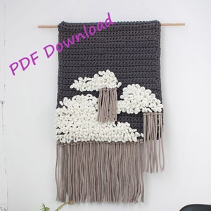 May include: A grey and white crocheted wall hanging with a cloud design. The hanging has a fringe border and is made with yarn.