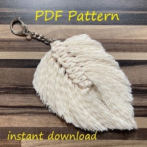 May include: A white feather keychain with a silver key ring. The feather is made of macrame and has a fringe. The text "PDF Pattern" and "instant download" is visible in the image.
