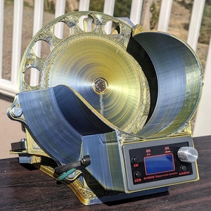 May include: A 3D-printed device with a gold and blue color scheme. The device features a circular, ornate design with multiple holes, a curved section, and a control panel with a screen and buttons. The text "ZK-SMC02 Stepper motor controller" is visible.