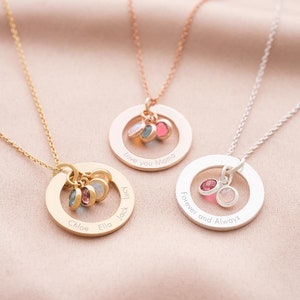 Three family eternal ring necklaces with engraving around rings and birthstones in the centre. One gold, one rose gold, one silver.