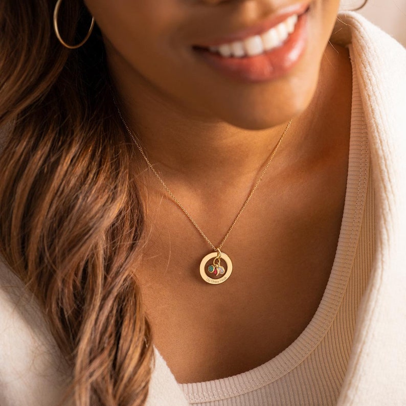 A model wearing a gold family eternal ring necklace with three names engraved around the ring and three birthstones in the centre.