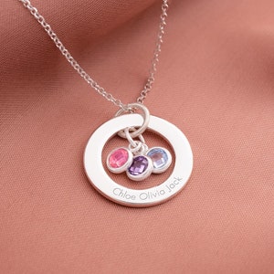 A silver family eternal ring necklace with three names engraved around the ring and three birthstones in the centre.