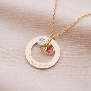 A gold family eternal ring necklace with three names engraved around the ring and three birthstones in the centre.