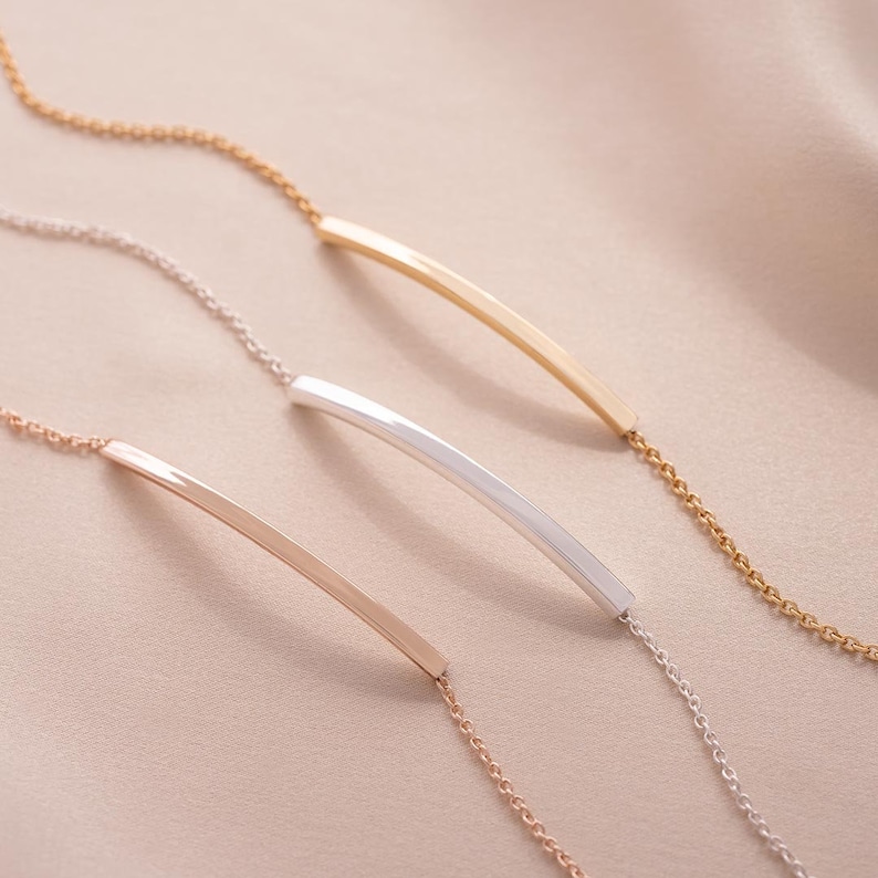 Three curved skinny bar bracelets from above One in rose gold, one silver, gold.