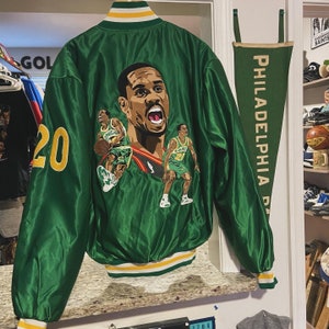 Könnte beinhalten: Grüne Satin-Bomberjacke mit Basketballspieler-Grafik auf dem Rücken. Die Jacke hat einen weiß, gelb und grün gestreiften Kragen und Bündchen, und die Nummer 20 ist auf dem Ärmel gestickt.