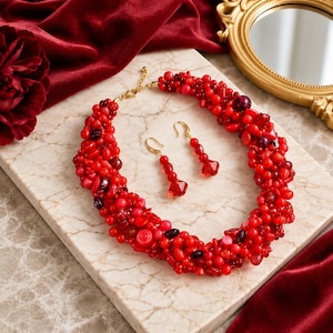 May include: A statement necklace and matching drop earrings set featuring a dense cluster of red beads in various shapes, sizes, and shades of red, including dark crimson and bright scarlet, finished with gold-tone metal hardware and clasps.