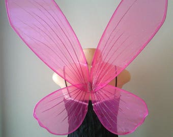 May include: Pink butterfly fairy wings with a sparkly finish. The wings are made of a sheer, translucent material and are attached to a black dress.