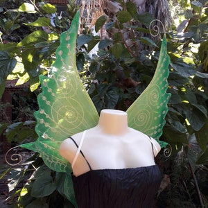 Peut inclure: Ailes de fée vertes avec des accents de paillettes dorées et une sangle blanche pour les attacher à un costume.