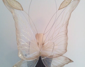 May include: A pair of sheer, white butterfly wings with gold glitter accents. The wings are attached to a wire frame and are designed for costume or cosplay.