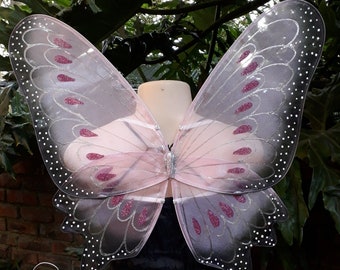 May include: Pink butterfly fairy wings with silver glitter and pink accents. The wings are attached to a wire frame and have a delicate, ethereal look.