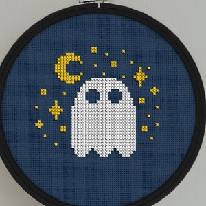 Op de afbeelding: Een witte geest op een blauwe achtergrond met gele sterren en een halve maan. De borduurwerk is in een ronde hoepel.