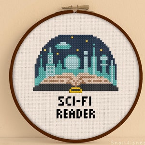 Peut inclure: Un cercle de broderie au point de croix avec un motif de science-fiction. Le motif comprend une ville, un livre ouvert et le texte "SCI-FI READER". Les couleurs sont le bleu, le turquoise et le marron.