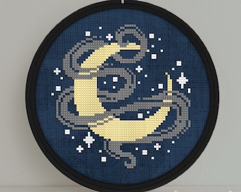 May include: A blue and yellow cross-stitch embroidery hoop with a crescent moon design and white stars on a dark blue background. The text "Snailfishes Stitches" is visible below the hoop.