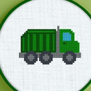 Puede incluir: Un patrón de camión de basura pixelado verde y gris en punto de cruz en un aro de bordado blanco.