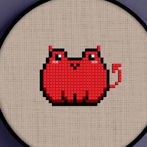 May include: Red cross-stitch embroidery of a cartoon cat with a devil tail, framed in a round hoop.