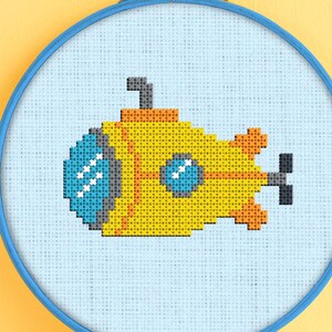 May include: A yellow submarine cross-stitch pattern in a blue embroidery hoop. The submarine has a small periscope and two round windows.