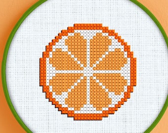 Könnte beinhalten: Ein Kreuzstich-Stickrahmen mit weißem Hintergrund und einem orangefarbenen Zitrusfrucht-Design. Das Design ist eine einfache, pixelartige Darstellung einer Orangenscheibe.