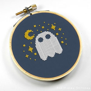 Op de afbeelding: Een witte geest met een halve maan en sterren geborduurd op een donkerblauwe achtergrond. De borduurwerk is in een hoepel.