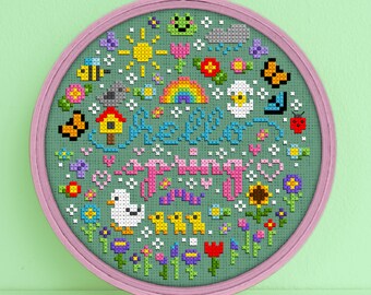 May include: A circular embroidery hoop with a green background and colorful pixelated embroidery. The embroidery features the text "Hello Spring" surrounded by flowers, butterflies, birds, and other spring-themed imagery.
