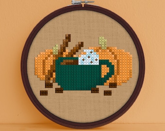 May include: Cross stitch pattern of a green mug filled with coffee, cinnamon sticks, and marshmallows, surrounded by orange pumpkins and coffee beans.
