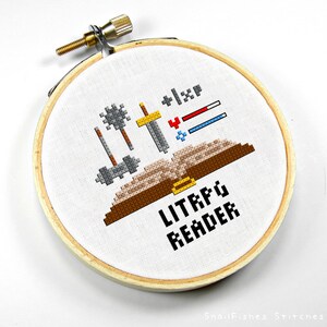 May include: A white embroidery hoop with a brown book, swords, and other weapons. The text "LITRPG READER" is below the book.