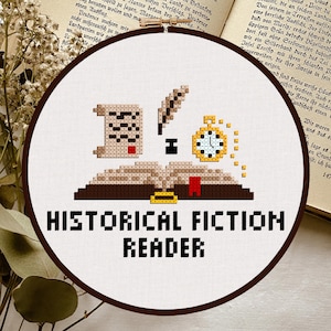 May include: A cross-stitch embroidery hoop featuring a design for a historical fiction reader. The design includes an open book, a scroll, a quill, and a pocket watch. The text "HISTORICAL FICTION READER" is stitched below the design.
